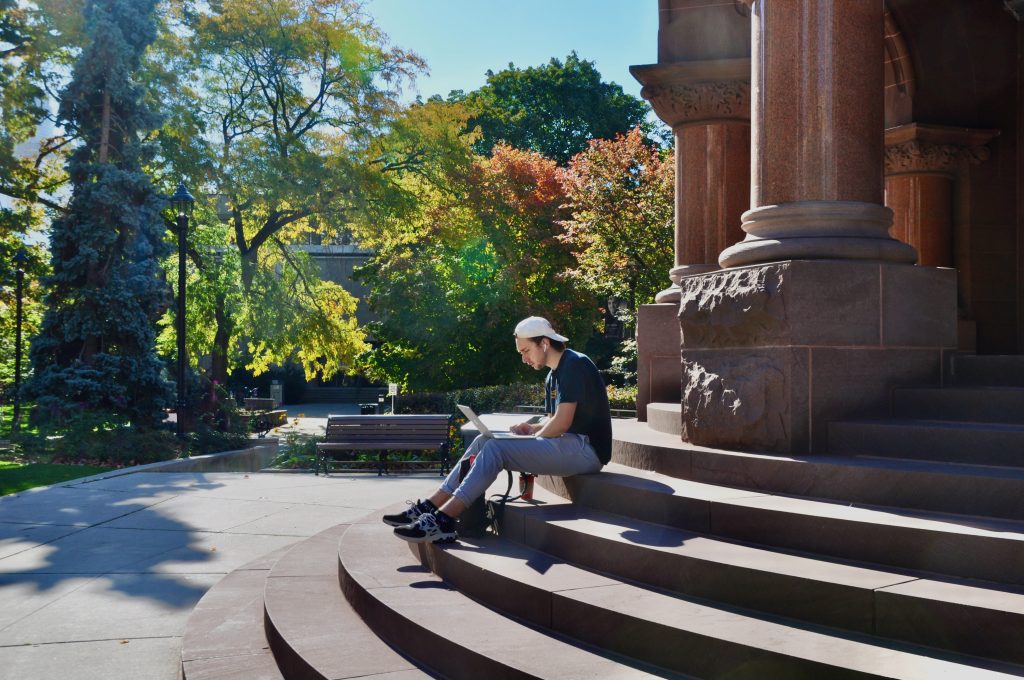 Student with laptop on the east entrance steps at Victoria College.