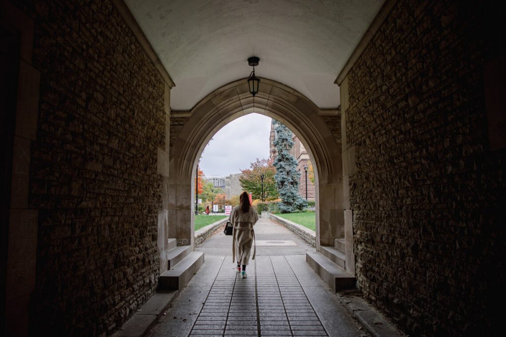 A student walking under an arch at Victoria College.