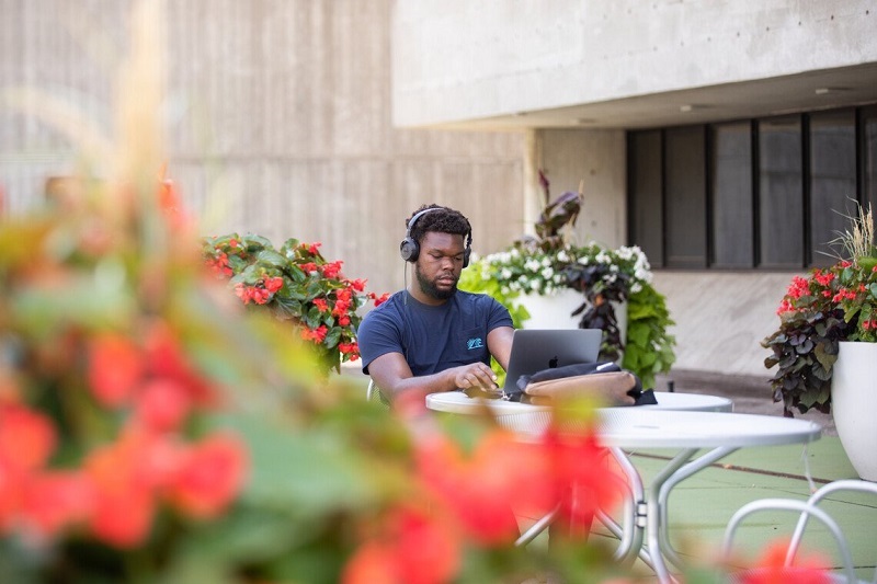 Student working on a laptop on an outdoor patio, flowers in the foreground