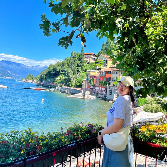Michelle pictured in front of a lake with greenery and colourful buildings behind her