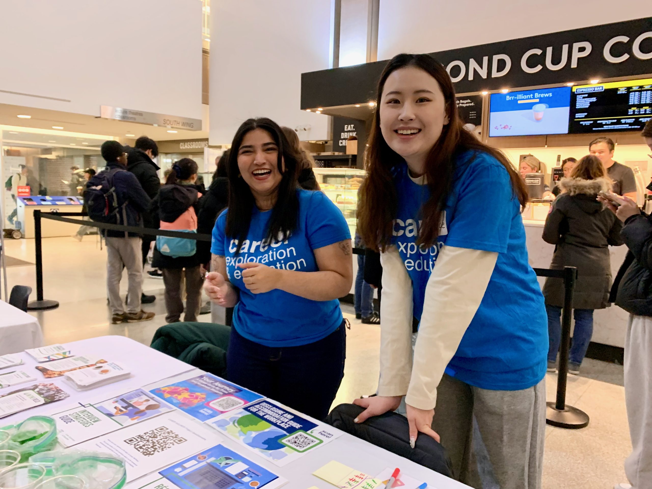 Volunteers smile at the camera at a desk covered with materials at the Program Exploration Fair